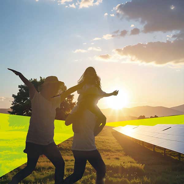 Eine Familie läuft bei Sonnenuntergang über ein Feld wo ein Solarparksrechts steht. Im Hintergrund sind Hügel zu erkennen.