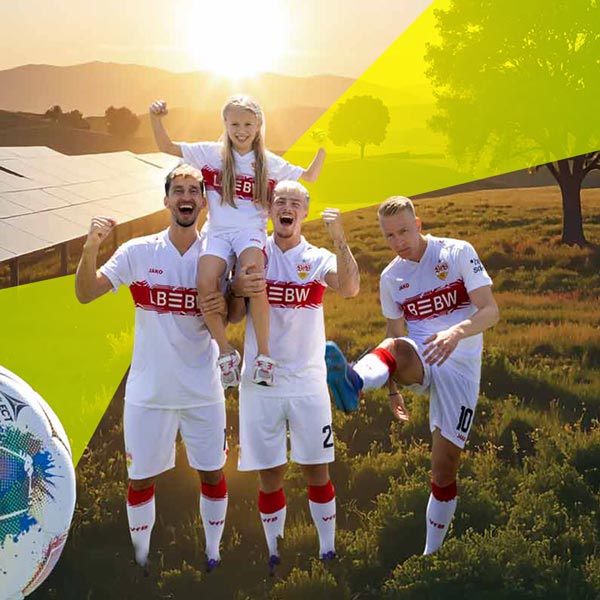 Drei VfB Stuttgart Fußballspieler stehen auf dem Feld und haben ein Mädchen mit demselben Trikot auf den Schultern. Der rechte Spieler kickt den Ball Richtung Kamera, der Ball ist vorne links angeschnitten. Im Hintergrund ist in der Landschaft, bei Sonnenuntergang, eine Solaranlage zu sehen.